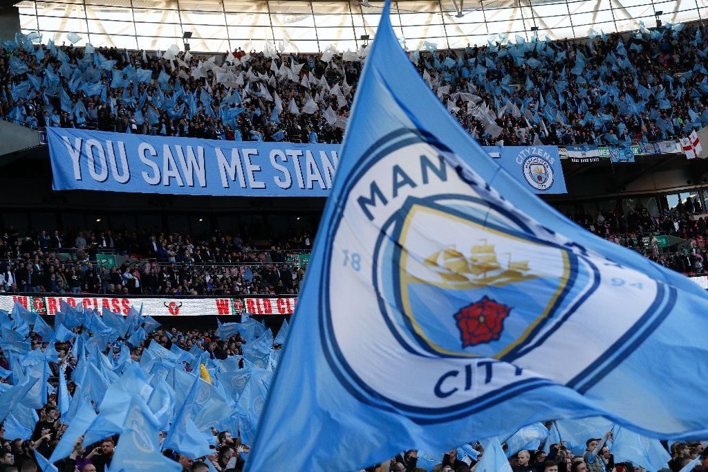 Manchester City fans citing at a stadium and watching their team play.